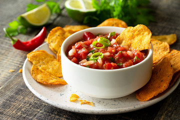 Tasty mexican nachos chips in bowl with salsa dip on wooden table.