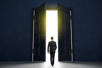 New life beginning concept with businessman entering open black doors in abstract bright space.