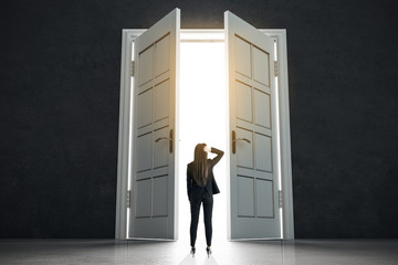Fototapeta premium Decision making concept with businesswoman standing in front of white doors in abstract bright space.