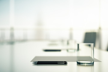 Close up of blurry conference table with glass, pen and blank sheet in the morning.