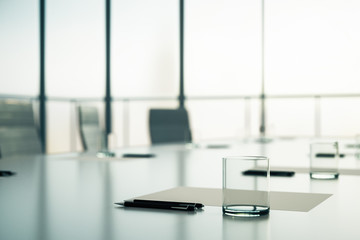 Close up of conference table with glass, pen and blank sheet at blurry window background in the...