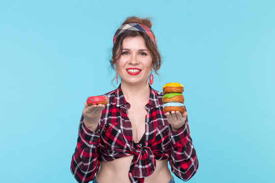 Charming young pin-up girl holding donuts in her hands and one posing on a blue background. Concept benefits and sales of sweets and baking.