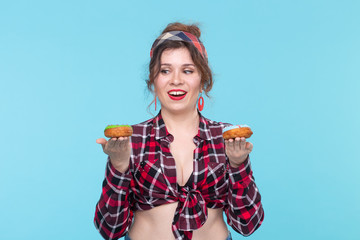 Positive young pin-up girl model holding in hands multicolored donuts posing on a blue background....