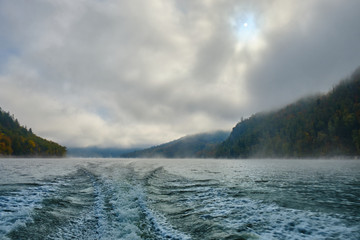 The trail of the boat (Wake) on a Norwegian lake in the middle of the mountains and fog in the autumn. Boat trip on the lake in autumn