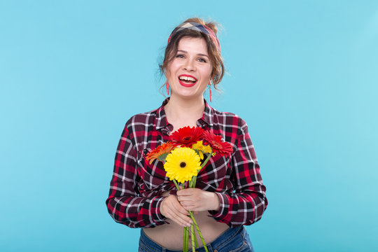 Beautiful positive young woman in a plaid shirt and a bandage sniffing beautiful bright gerbera flowers posing over a blue background. Concept of gifts and greetings.