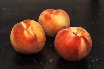 Three tender ripe peaches on a black background close-up