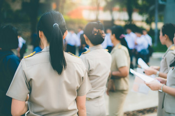 The female high school teachers in Thai government teacher uniform are holding documents, checking student names and standing among students, Thailand, southeast Asia.