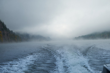 Walk on the Norwegian lake on a boat in the autumn in the fog. Wake of the boat