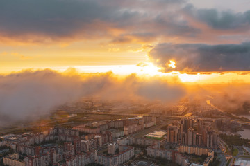 Urban cityscape, aerial top view with low flying clouds over a residential area of the city, view of the horizon and the dawn of the sun.