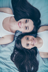 Vertical close-up top above high angle view portrait of two nice-looking beautiful attractive lovely tender sweet charming feminine shine cheerful cheery people spending free time lying on blue linen