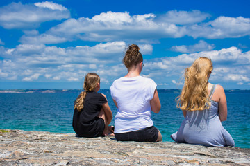 Fototapeta premium three girls photographed from behind while they are looking to the ocean in Camaret-sur-Mer in France