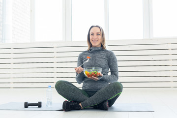 sport, healthy, people concept - Girl holding salad and dumbbell after fitness training