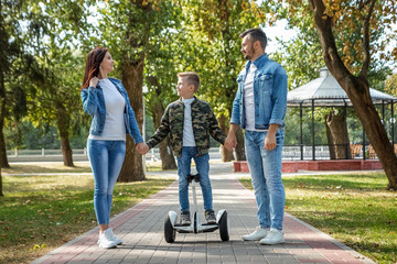 Modern family, dad mom son rides a hoverboard in the park, self-balancing scooter. Active lifestyle technology future