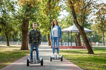 Fototapeta premium Mom and son ride a hoverboard in the park, a self-balancing scooter. Active lifestyle time with baby technology future