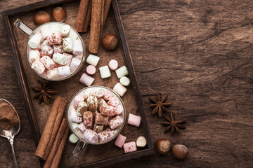 Hot winter or autumn drink with cocoa, chocolate, spices and marshmallows in cups on vintage wooden background top view