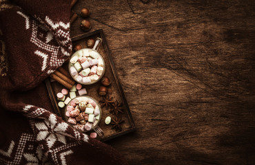 Fototapeta na wymiar Hot winter or autumn drink with cocoa, chocolate, spices and marshmallows in cups on vintage wooden background with knitted warm sweater, top view