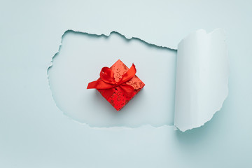 Gift with a red bow on the background of a big hole on a paper background mint color. Minimalism. Holiday concept. Flat layout. Copy space.