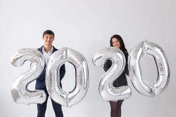 New year, celebration and holidays concept - love couple having fun with sign 2020 made of silver balloons for new year on white background
