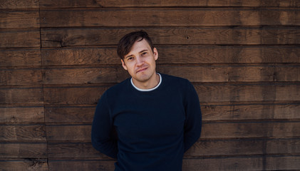 A handsome man in a blue sweater poses against a wooden background