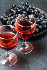 Red wine in glasses, a bunch of black grapes. Dark background.