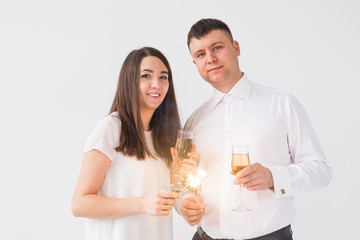 New year, holidays, date and valentines day concept - Loving couple holding sparklers light and glasses of champagne over white background