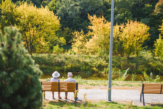 An elderly couple enjoying the view of nature on a beautiful autumn day while sitting on a bench next to a river