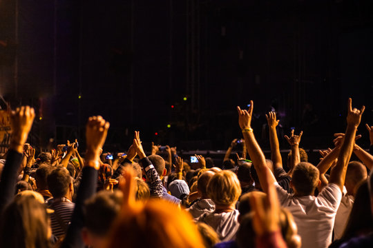crowd of people with hands up standing at a street music concert and taking pictures on a phone show, blurred background