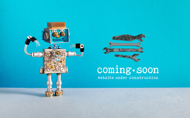 Web site under construction Coming Soon template page. Toy robot looks at a set of hand wrenches for maintenance repairs and service works. Blue wall and copy space on gray background. - 290087769