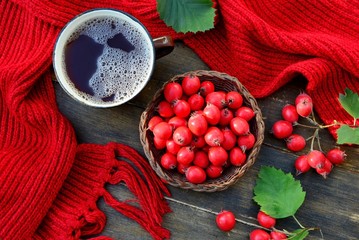 Hawthorn berries and drink in a mug with a red scarf on a wooden table top view
