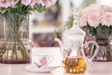 Teapot and cup with blooming tea flower and pink Chrysanthemum flowers in glass vase on table.