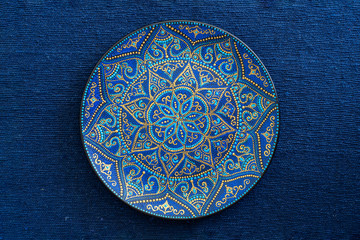 Decorative ceramic plate with blue and golden colors, painted plate on the background of blue...