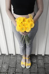 Women holding beautiful bouquet of yellow flowers (Gerbera). Dressed in black and white during Summer. Yellow shoes and green nail polish.