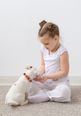 Childhood, pets and dogs concept - Little puppy and child girl in white shirt having fun