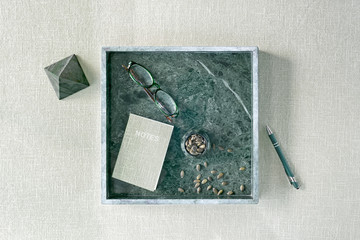 Minimalist stationery set in green marble square tray on canvas background.