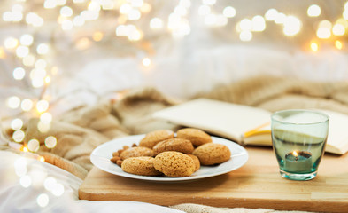 food, bakery and hygge concept - oatmeal cookies on plate and candle in holder at home