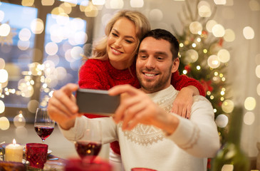 christmas, holidays, technology and people concept - happy couple in taking selfie by smartphone at home dinner