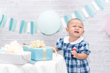 Beautiful smiling one year old cute baby girl standing near the gift box on family party.