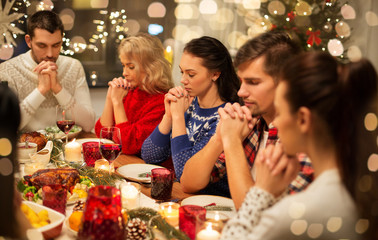 holidays and celebration concept - friends holding hands and praying while having christmas dinner at home