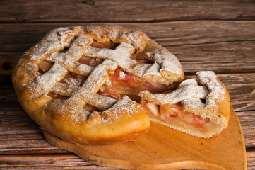 Home cooking. Appetizing Apple pie with sliced on wooden background.