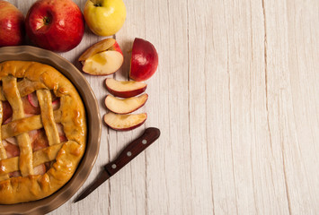 Homemade cake. Delicious Apple pie in ceramic form, knife, sliced red apples on a light wooden background.