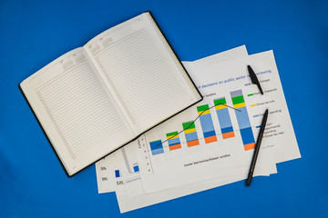 a pile of documents along with a notebook and pen lying on the blue table.