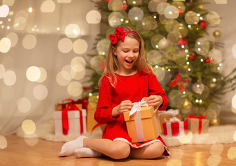 christmas, holidays and childhood concept - smiling girl in red dress with gift box at home