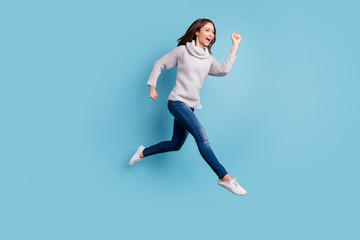 Fototapeta na wymiar Full size profile side photo of excited candid teen run jump have free time wear knitted sweater pullover denim jeans sneakers isolated over blue color background