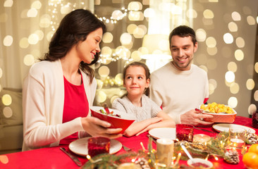 holidays, family and celebration concept - happy mother, father and little daughter having christmas dinner at home