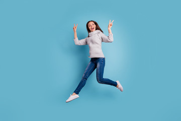 Fototapeta premium Full size photo of crazy content carefree girl jump make v-signs scream feel excited rejoice wear knitted pullover sweater good look denim jeans sneakers isolated over blue color background