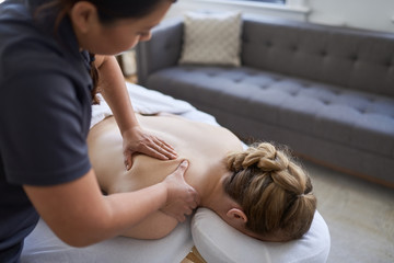 Chinese woman massage therapist giving a treatment to an attractive blond client on massage table in a bright medical office