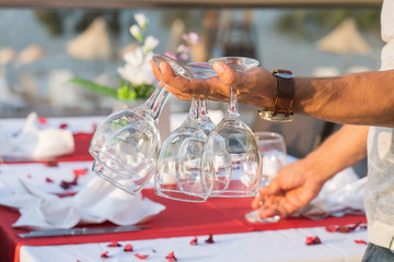 The waiter holds wine glasses in his hand and sets the table in a restaurant . Nice dining table set with arranged silverware and napkins for dinner, Turkey