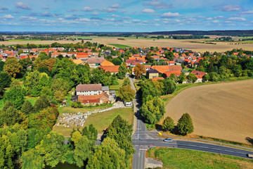 Obraz premium Aerial view of an intersection of country roads in front of the entrance to a small village in the flat landscape of Northern Germany