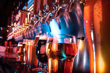 Glasses of dark and light beer, ale, lager, stout, porter in modern and bright neon light with pouring machine on background. Concept of holiday, fun, meeting, oktoberfest, big friends' party. - obrazy, fototapety, plakaty