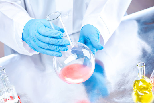 The laborant is holding a vessel with a chemical liquid. Analysis of the composition of detergents. Experiments in the chemical laboratory. Chemist in gloves and a white coat conducts the experiment